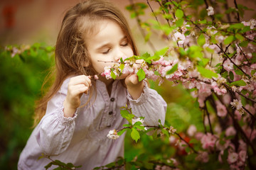 small girl in garden sniffs almond bush 