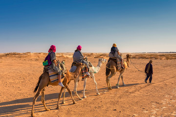three people in Berber national robes on camel guided camels