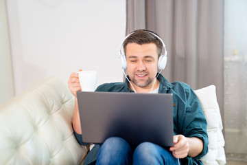 man listens audio with headphones on sofa