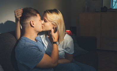 Close up photo of a caucasian couple kissing and embracing on the sofa late evening