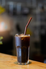 Close up plastic take away cup of iced black coffee served with milk, sugar syrup and butter cookies on wooden 