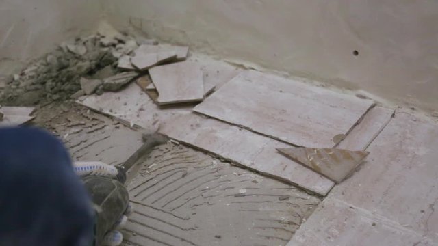 Worker removing old tile from the floor in bathroom