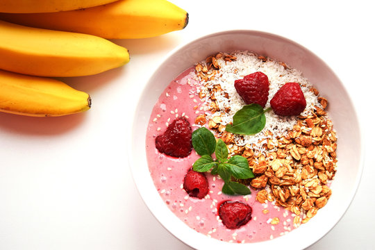 Pink Smoothie With Granola And Raspberries And Bananas On A White Background