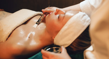 Caucasian female lying while masseur applies a transparent facial body mask at the wellness center