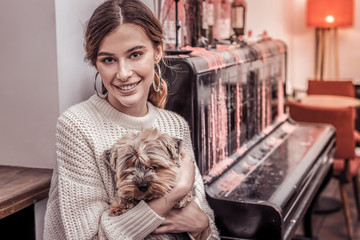 Happy beautiful woman sitting in cafe holding her small dog