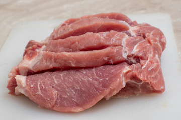 Close-up of several steaks, pieces of pork on a white cutting board