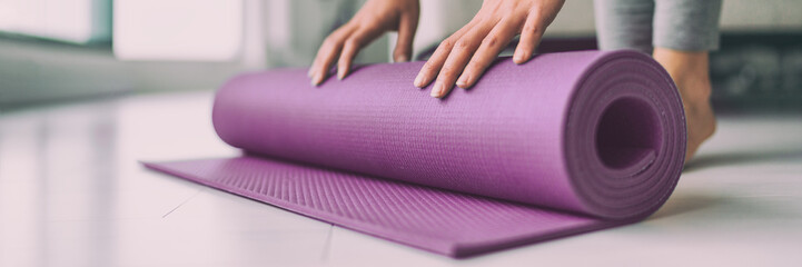Yoga at home woman rolling pink exercise mat in living room starting warm up meditation zen well being wellness banner panoramic apartment living room lifestyle.