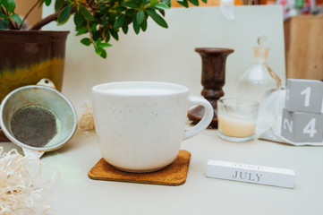 cozy home workplace with a Cup of matcha with milk foam on a natural stone stand, a green home plant and a wooden perpetual calendar with an inscription June July