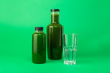 Fresh celery spinach juice in a plastic and glass bottle and an empty glass nearby, isolated on a green background. Healthy diet detox juice.