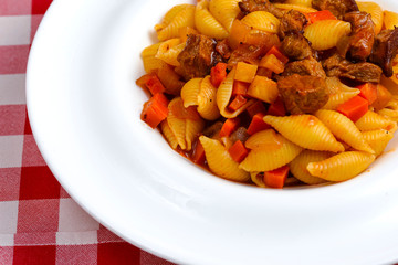 Macaroni pasta with meat pieces in tomato sauce and vegetables in bowl. Top view.