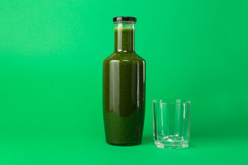 Fresh celery spinach juice in a glass bottle and an empty glass near isolated on green background. Healthy eating Detox juice diet.