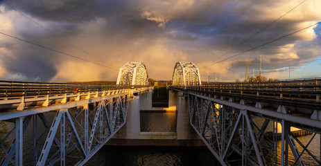 truss railway bridges suspended over the river leading directly to a dramatic evening storm