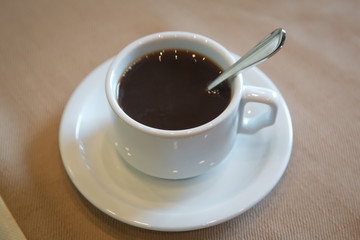 Cup of hot coffee on table in cafe white background . coffee beans in white porcelain cup decorated wild herbs . white cup, coffee in white sauce.