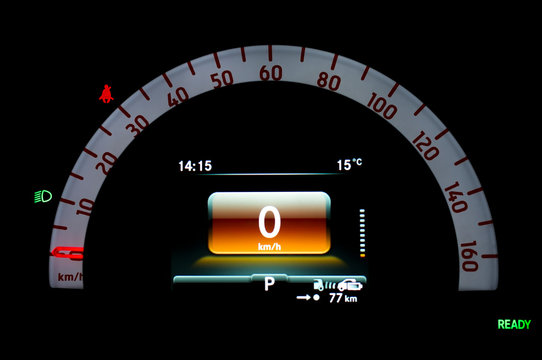Close up of illuminated circular speedometer in full electric vehicle. Car cluster with analogue and digital speed gauge. Instrument panel with seat belt reminder and dipped beam headlights icon. - Powered by Adobe
