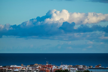 Obraz premium Beautiful blue coloured background of sea ocean water and horizon line with white clouds in the sky and coloured houses on the town coast - concept of travel tourism and nature