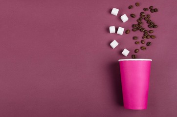 Top view of pink paper cup. coffee beans, sugar cubes on the dark red surface.Empty space for design, decoration.Concept of preparing classic coffee