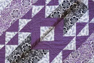 Purple coloured handmade patchwork bed quilt with various fabric geometric designs