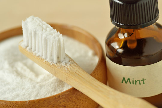 Baking soda in a bowl with a wooden toothbrush and peppermint essential oil - Homemade natural toothpaste