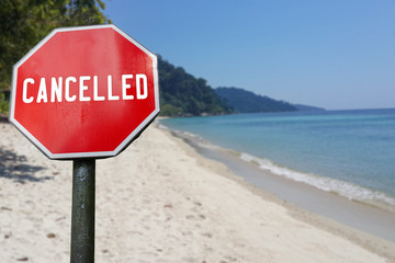 Red cancelled sign on beach background. COVID-19 pandemic quarantine. Cancelled vacation, travel, holiday plans because of corona virus.