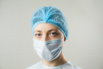 Strict woman doctor in a protective medical mask on his face and surgical hat. Fatigue in the eyes. Tired person. Caucasian young specialist. Stern look. On white background