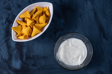 sour cream in a transparent bowl, chips on a white plate, blue abstract background