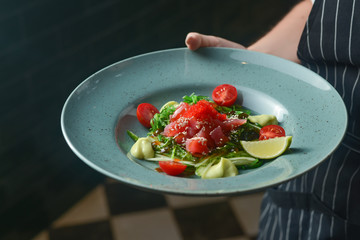 Waiter serving food in a restaurant. Sea food salad with salted fish, sesame seeds, red caviar, cherry tomatoes, lime.