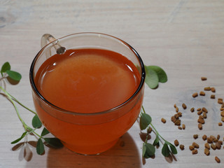 Healing drink, seeds, green sprig of the medicinal plant fenugreek on a wooden light table...