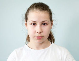 Young Caucasian girl with a neutral expression on her face. Portrait on grey background, emotions...