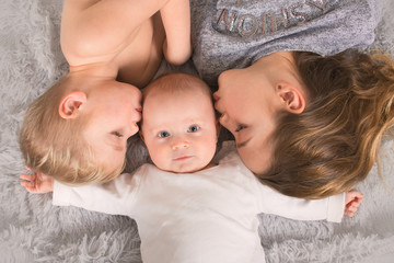 young siblings laying on the furry blanket and kissing their little brother, brothers and sister...