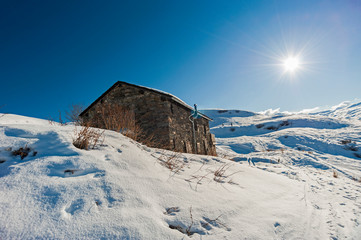 Panoramic view across snow covered slope on alpine mountain with small house - Powered by Adobe