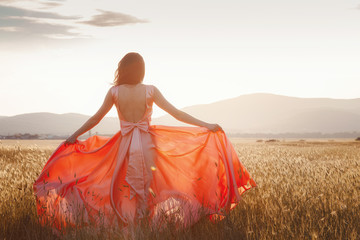 Fototapeta na wymiar girl dancing in a field in a beautiful pink dress at sunset