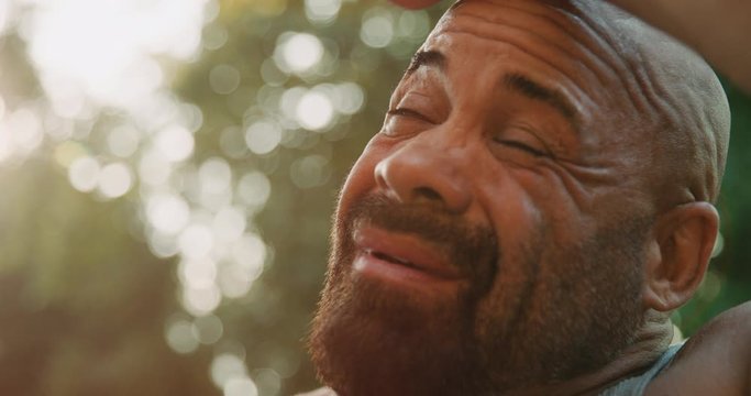 Bald, tan, muscular man wiping sweat and drinking water on a hot day.
