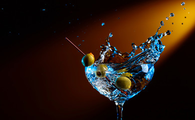 Glass of martini with green olives. Cocktail in glass with splashes.