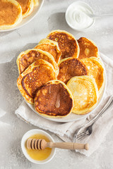 Homemade pancakes with honey and sour cream, sunny shadowed table surface. Light grey concrete background. Natural light and shadows food photography concept. Breakfast.