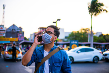 Concept, diseases, viruses, allergies, air pollution. Man wearing surgical mask on street while using phone. The image face of a young man wearing a mask to prevent germs, toxic fumes, and dust. 