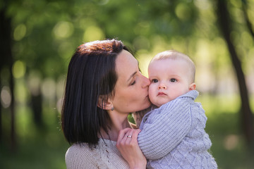 A beautiful mother holds her little son in her arms. A mother hugs her son - mother’s love and protection. A young woman with a child walks in the park. Life before and after the global pandemic.