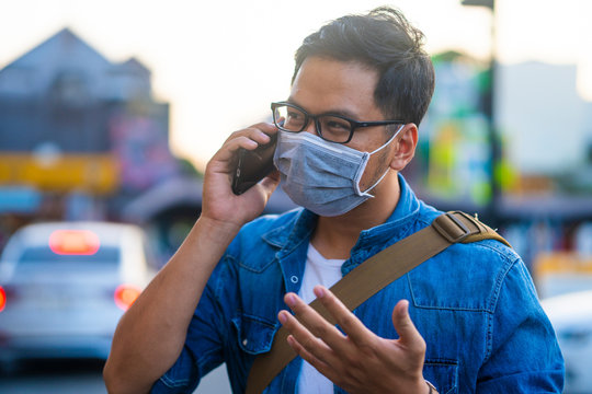 Concept, diseases, viruses, allergies, air pollution. Portrait of Man wearing surgical mask on street while using phone. The image face of a young man wearing a mask to prevent germs, toxic fumes...