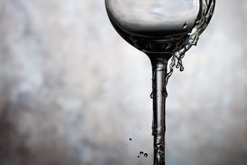 Naklejka na ściany i meble Motion of pouring splash water in transparent wine glass. Water splashing out of a tall wine glass.