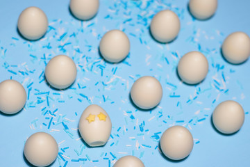 A pattern of chocolate eggs with one special egg sprinkled with sweet powder. One egg with eyes in the shape of stars and tilted sideways. The photo was shot close-up on a pale blue background.