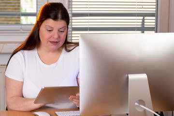 Professional woman working at home. She has a computers on her desktop and a tablet in her hand.