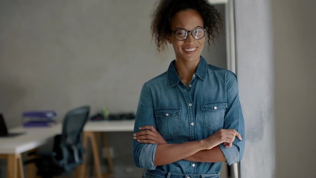 Businesswoman standing in the office. Woman in casuals standing by the window in the office looking at camera and smiling.
