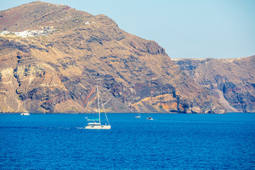 Sailboat in the sea over beautiful big mountains background, luxury summer adventure, active vacation in Santorini, Greece