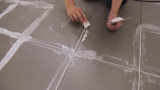 Worker troweling joints between tiles on floor