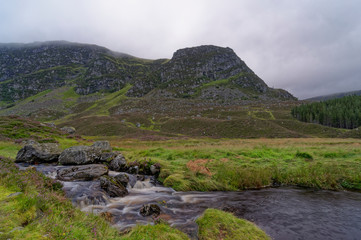 A small river flowing through Corrie Fee, with low cloud and morning mist covering the Hill Tops.