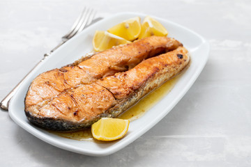 fried salmon with lemon on white dish on ceramic background