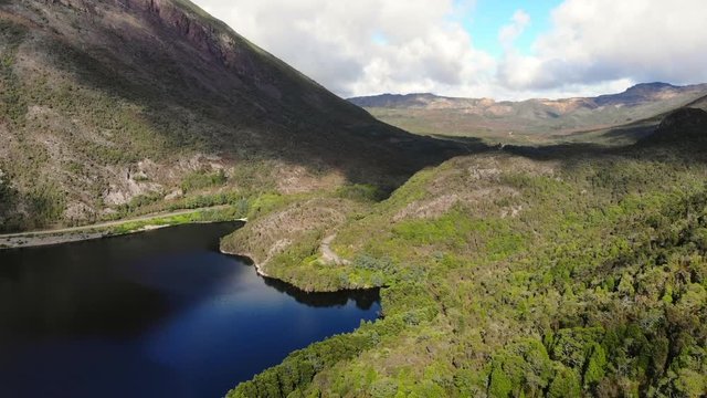 Drone pan up of Tasmanian lake with mountains and blue sky with clouds around. Shadow of clouds on the mountain side with dark lake below