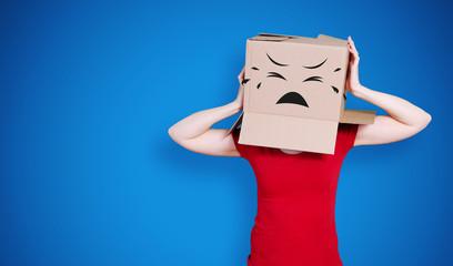 Person with cardboard box on its head and a sad face expression holding its head on dark blue background