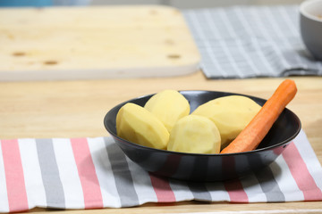 fresh peeled potatoes and carrot in a black plate with kitchen towel on a wooden table. Vegetarian breakfast . Vegan lunch. Vegetarian lunch.