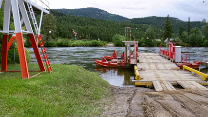 Obraz na płótnie Canvas red ferry crossing the mountain river on the forest and hills background, British Columbia, Canada.