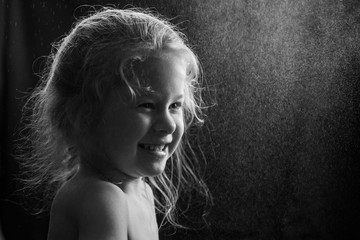 black and white frame: portrait of a little girl under the spray on a black background